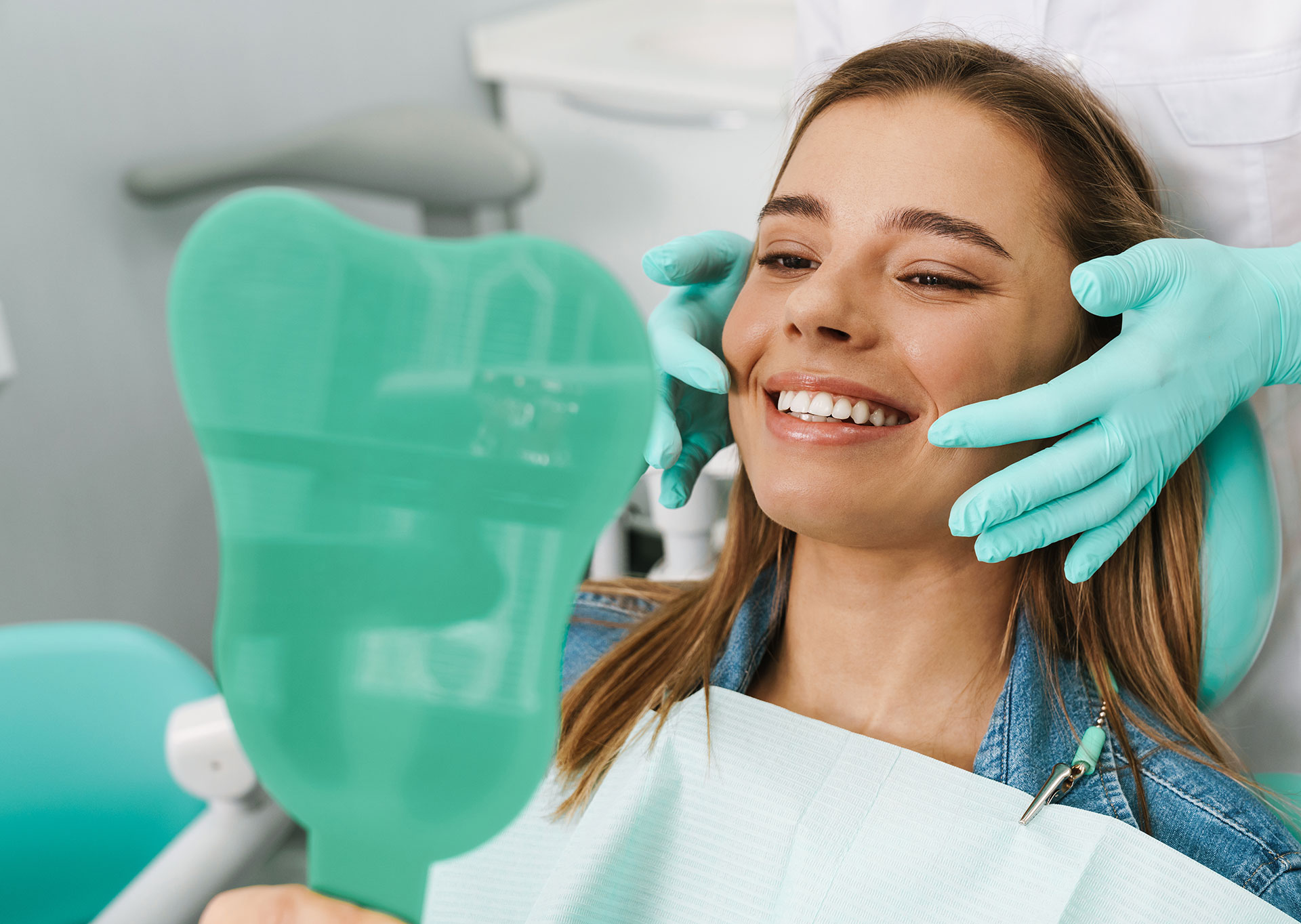 A woman in a dental chair, smiling at the camera, with a dentist s hands holding up a clear plastic model of teeth.