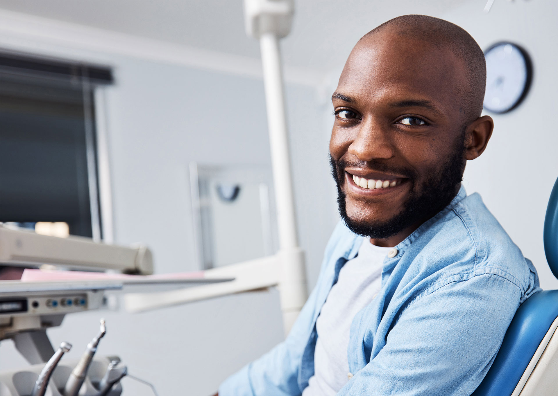 A man, possibly a dental professional, is smiling and sitting in front of a dental chair.