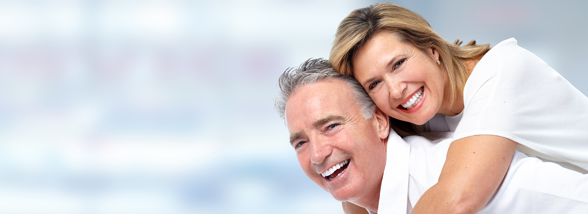 An elderly couple smiling and embracing each other against a blurred background.