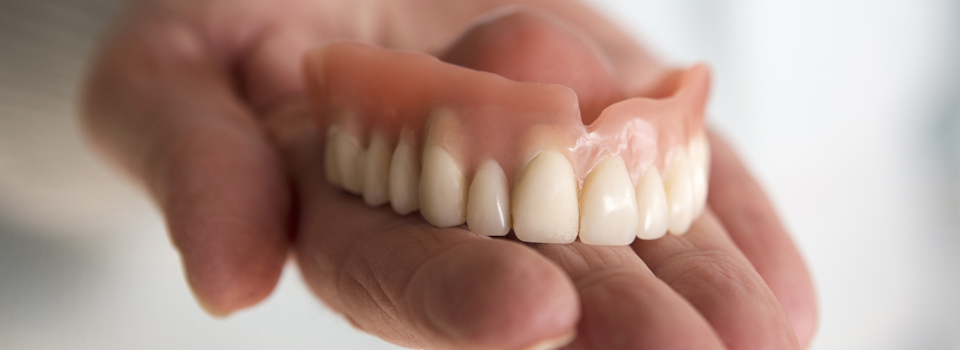 The image shows a person holding an artificial set of teeth, which appear to be dentures, with the teeth facing upwards.