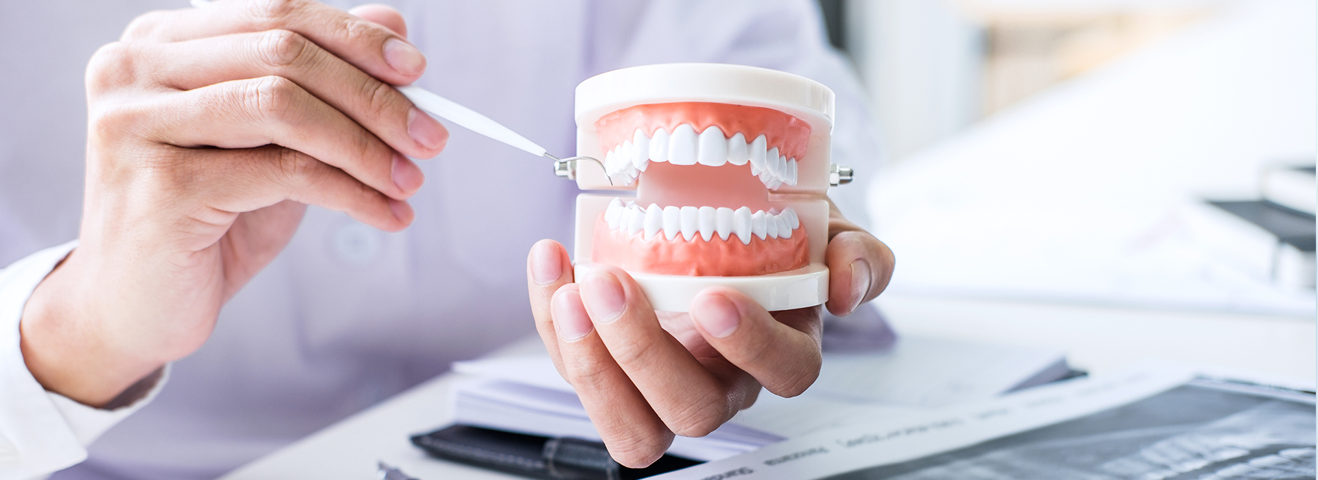 A person s hand holding a toothbrush with a toothpaste tube in the background, suggesting dental care or oral hygiene.