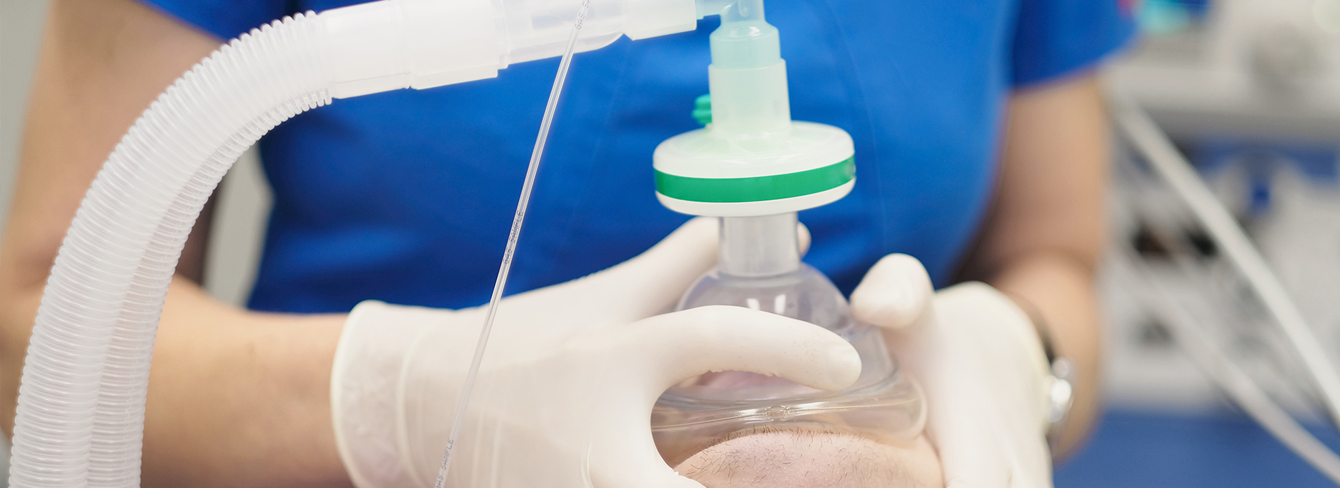 The image shows a person wearing gloves and a mask, handling a clear plastic container with a transparent green substance inside.