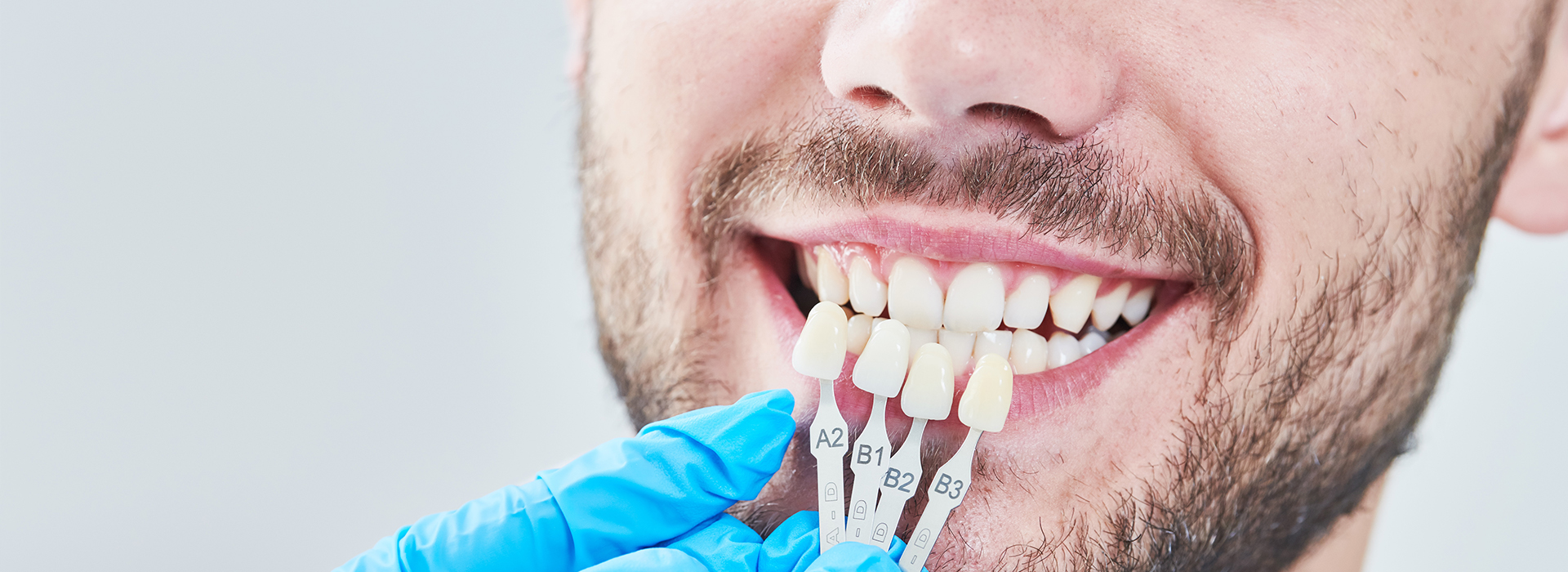 A person with a smile, wearing a blue surgical mask and holding dental implants.