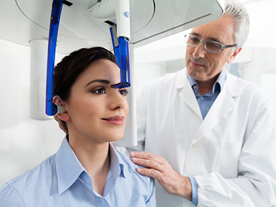 A woman in a blue shirt receiving an MRI scan, with a medical professional standing beside her and adjusting the scanner.