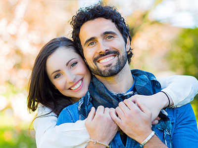 The image shows a man and a woman smiling at the camera, with the man wearing a blue t-shirt and the woman in a white top. They appear to be a happy couple.