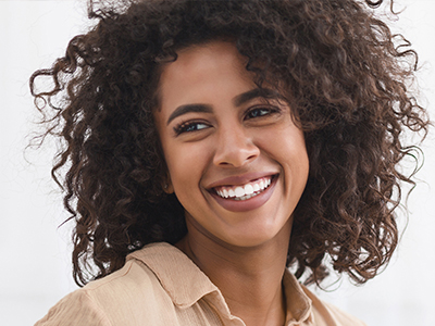 A smiling woman with curly hair and a radiant smile, wearing a beige top.